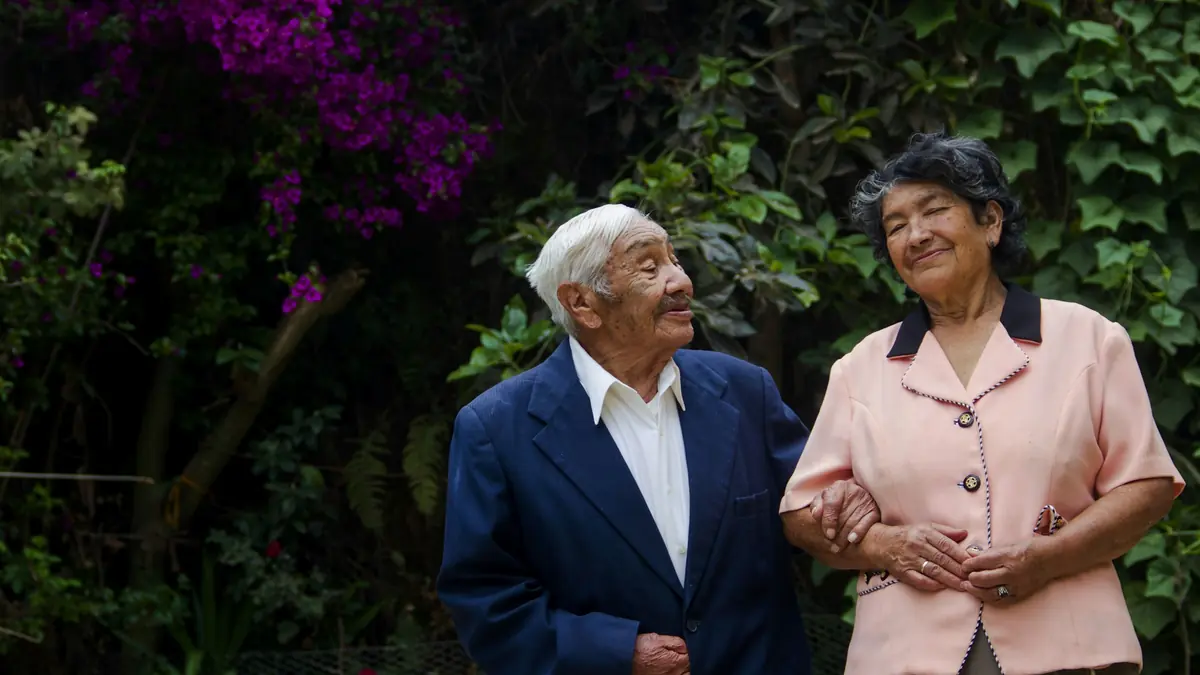 Una pareja de adultos mayores, del brazo y sonriente, en un jardín