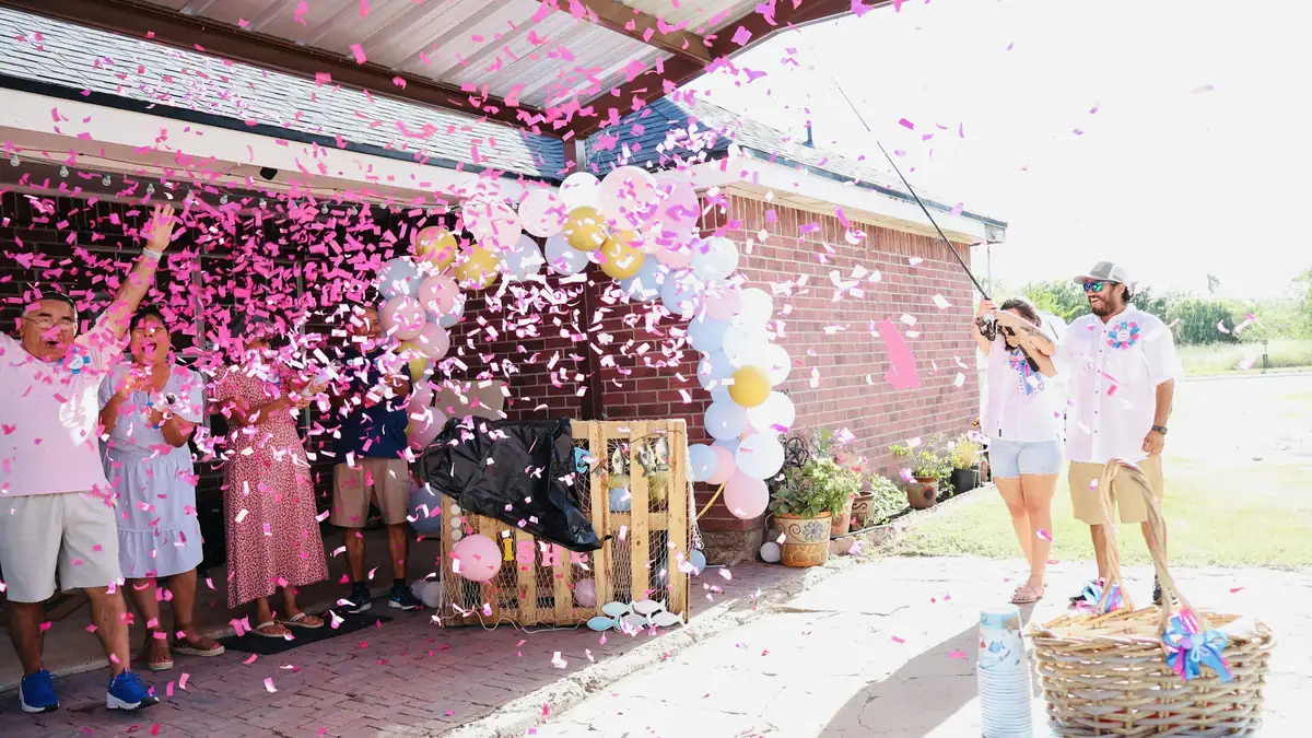 A family bursts pink confetti outdoors at a gender reveal