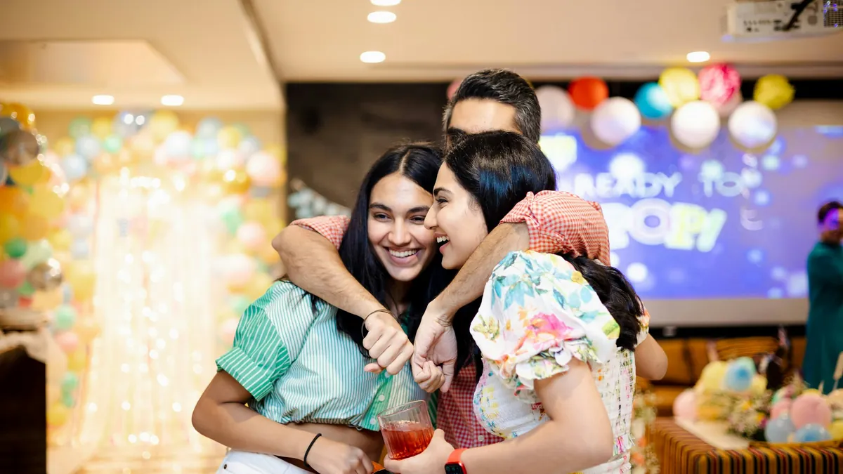 Friends hug and laugh at a baby shower decorated with balloons