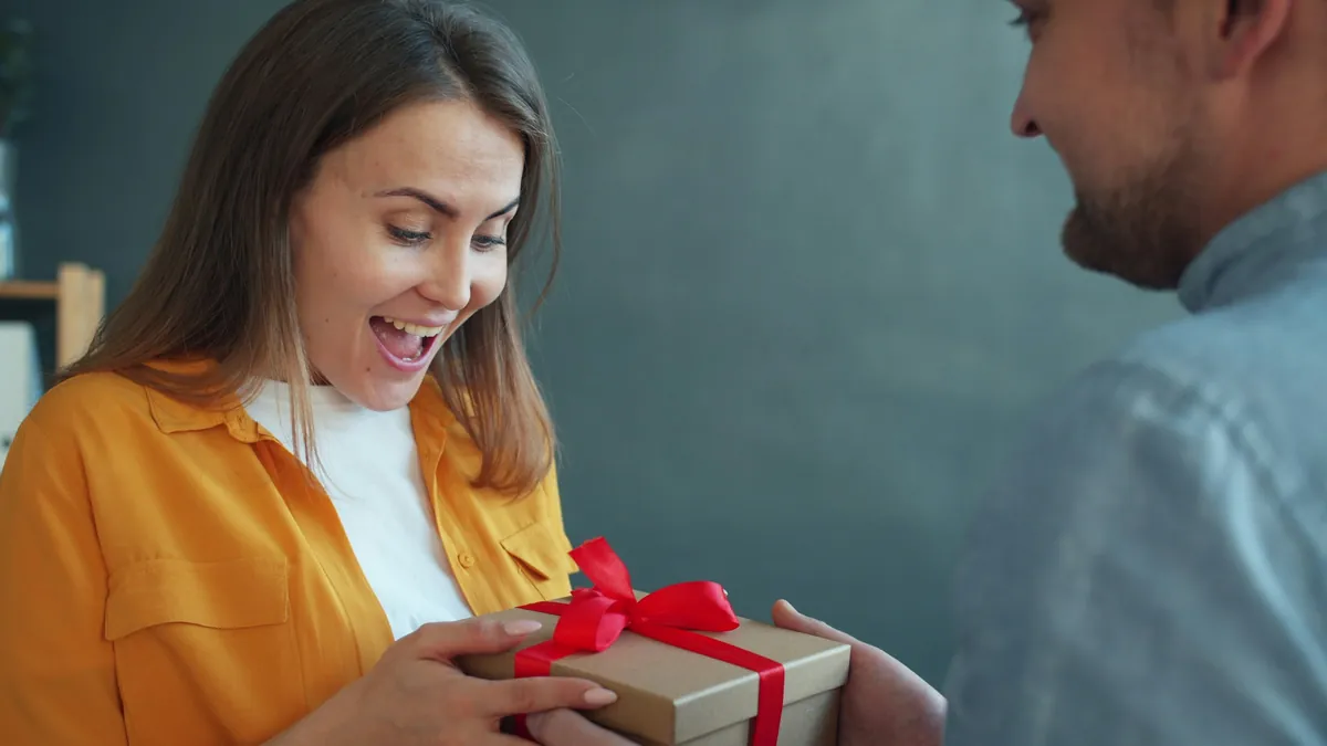 Una mujer sonríe sorprendida al recibir un regalo con cinta roja