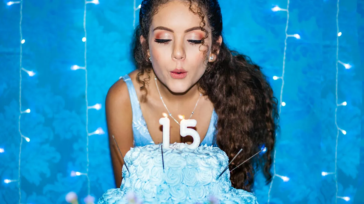 Una quinceañera sopla la vela del 15 en su torta celeste