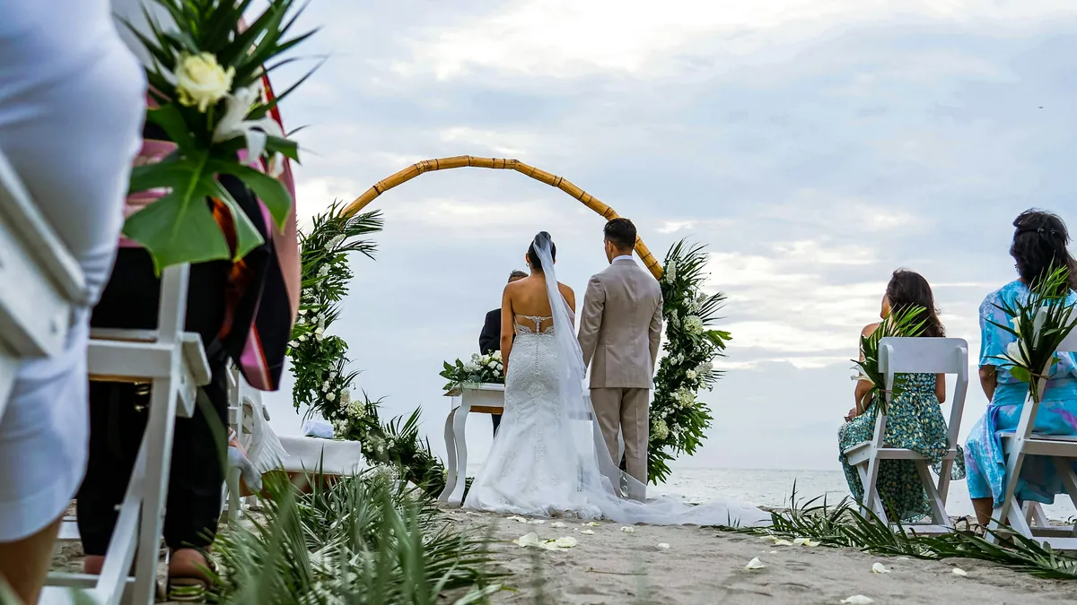 Los novios frente al arco de flores en una ceremonia en la playa de Máncora, con los invitados sentados