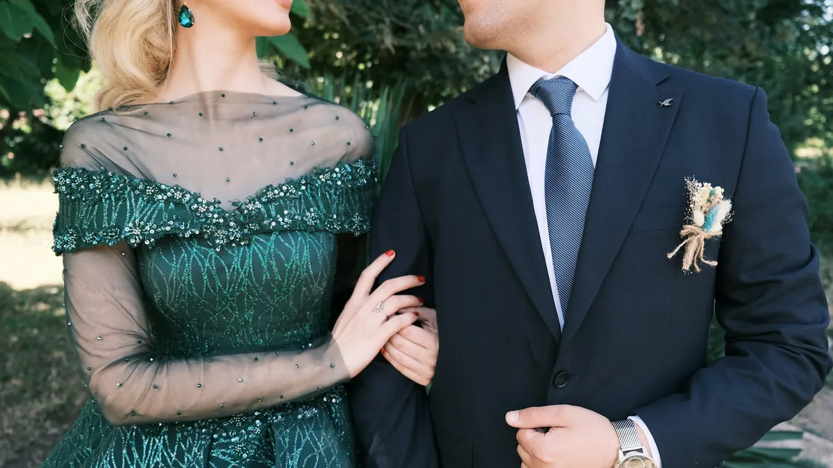 Una pareja de invitados vestida de gala: ella con vestido verde bordado y él con terno azul