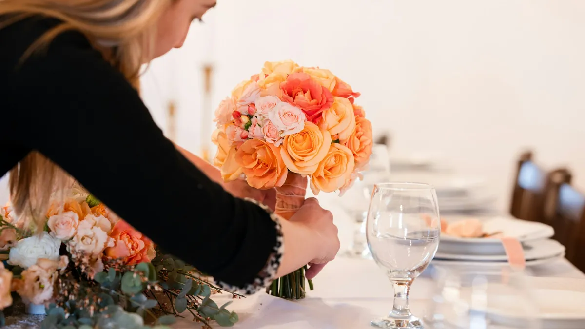 A decorator places a bouquet of orange roses on a wedding table