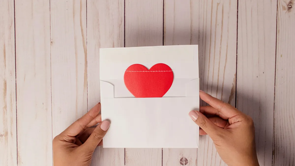 Dos manos sostienen un sobre blanco con un corazón rojo