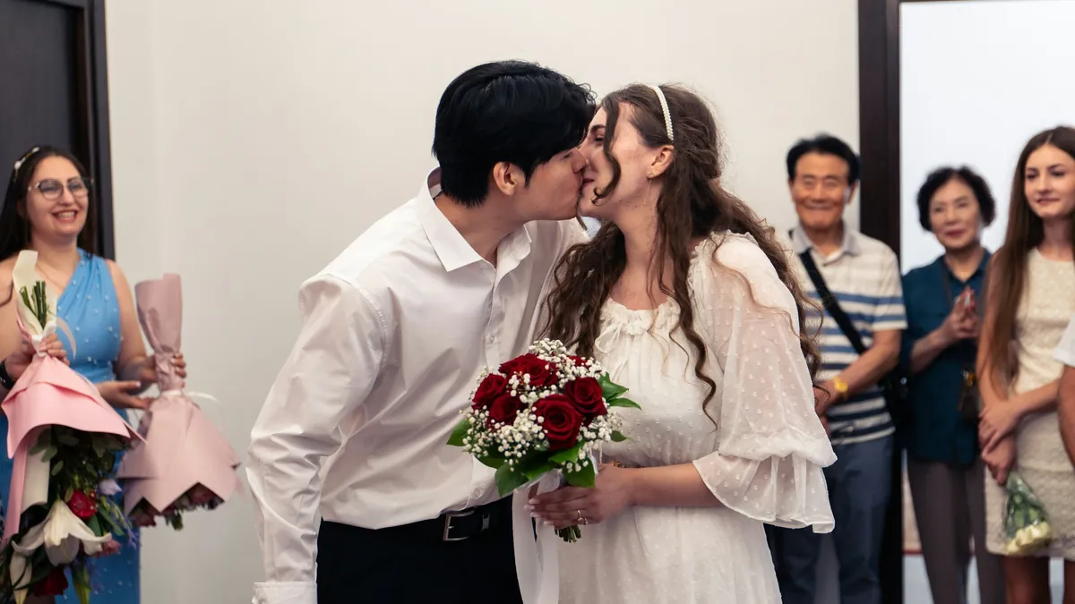 Los novios se besan en su matrimonio civil mientras la familia los mira con flores en las manos