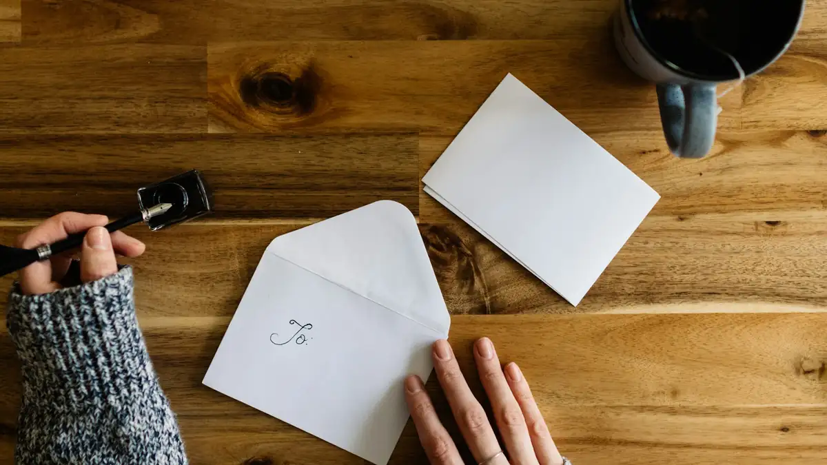 Hands open an envelope beside a card on a wooden table