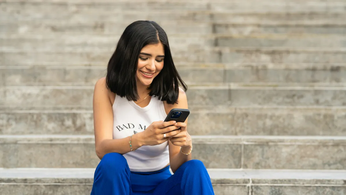 A young woman smiles at her phone while sitting on some steps