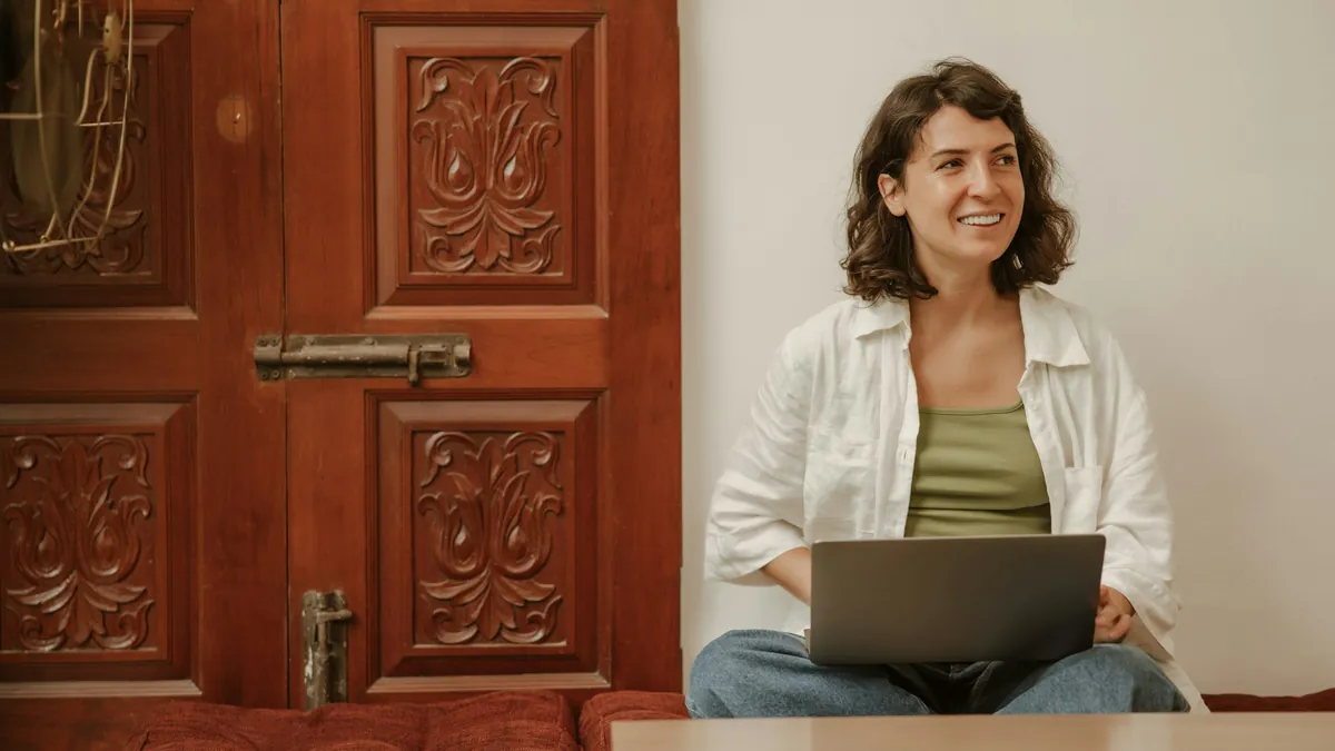 A woman smiles with her laptop on her lap at home
