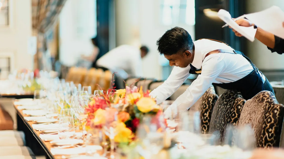 Un organizador arma una mesa larga de banquete con flores y copas