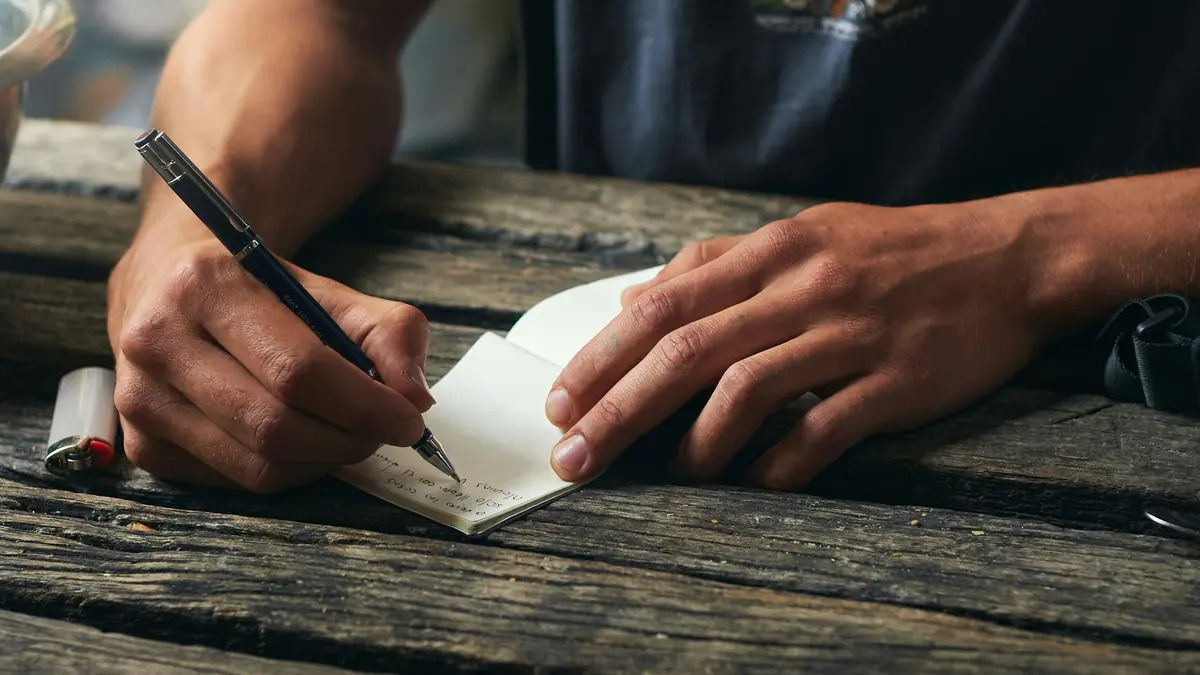 Unas manos escriben a mano dentro de una tarjeta sobre una mesa de madera