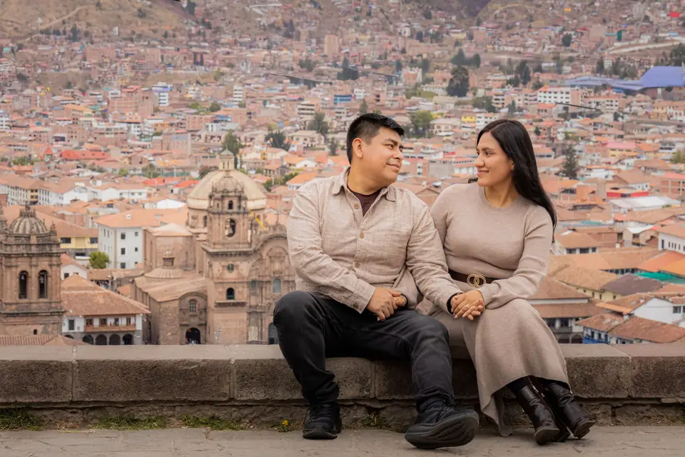 A couple sitting at a lookout, with the rooftops of Cusco and its cathedral behind them