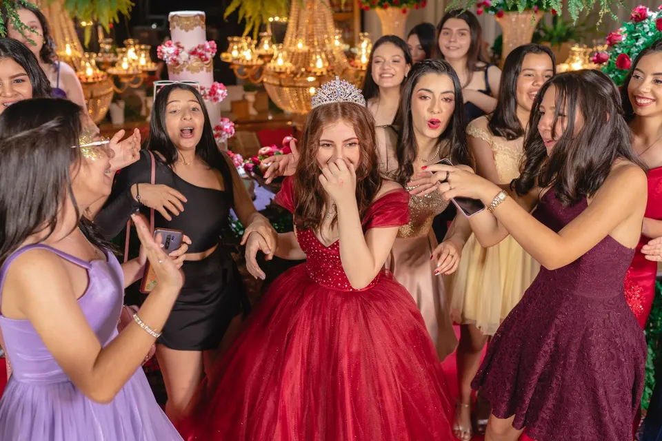 La quinceañera, con corona y vestido de fiesta, rodeada de sus amigas emocionadas
