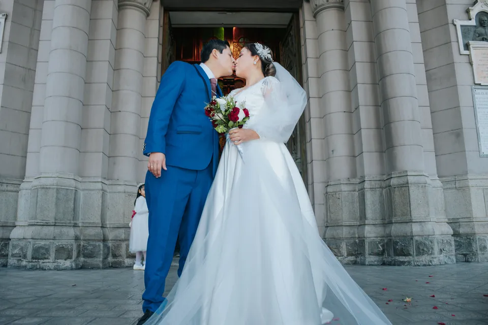 The newlyweds kiss outside the church in Lima, bouquet in hand