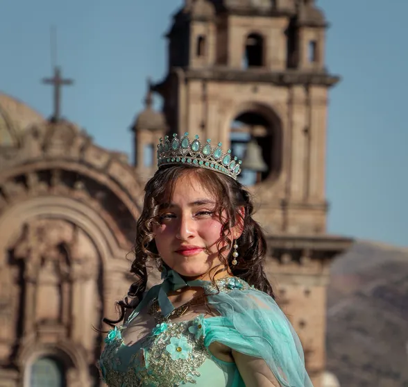 A quinceañera in a tiara and a turquoise gown in front of a church in Cusco