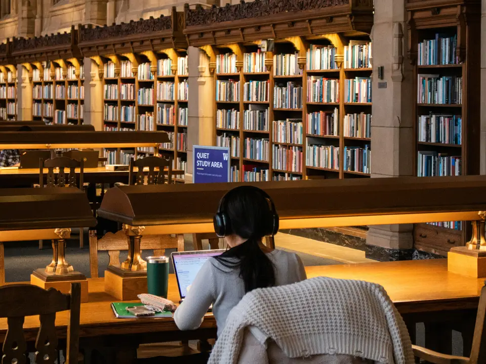 A student wearing headphones works on her laptop in an old library