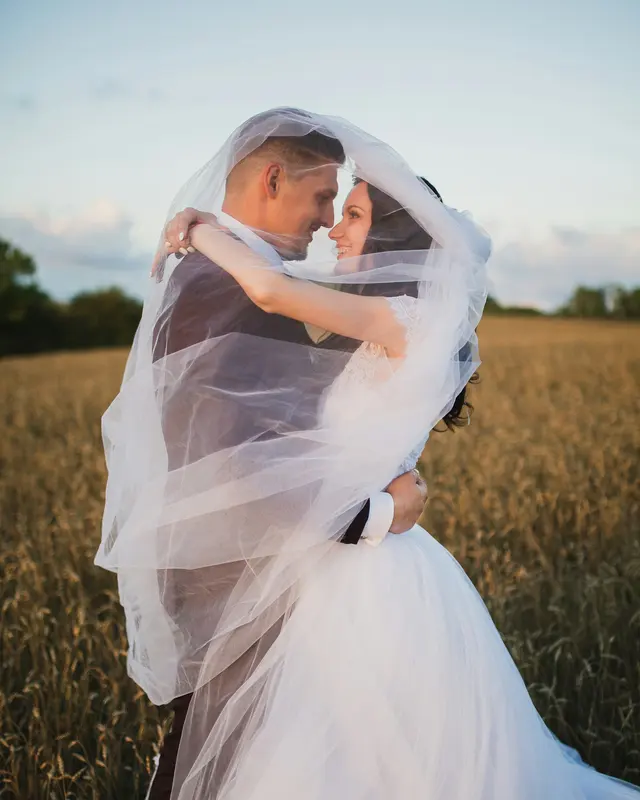 Newlyweds embracing beneath a veil outdoors